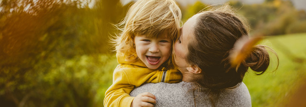 A mother kisses her daughter on the cheek while standing outdoors