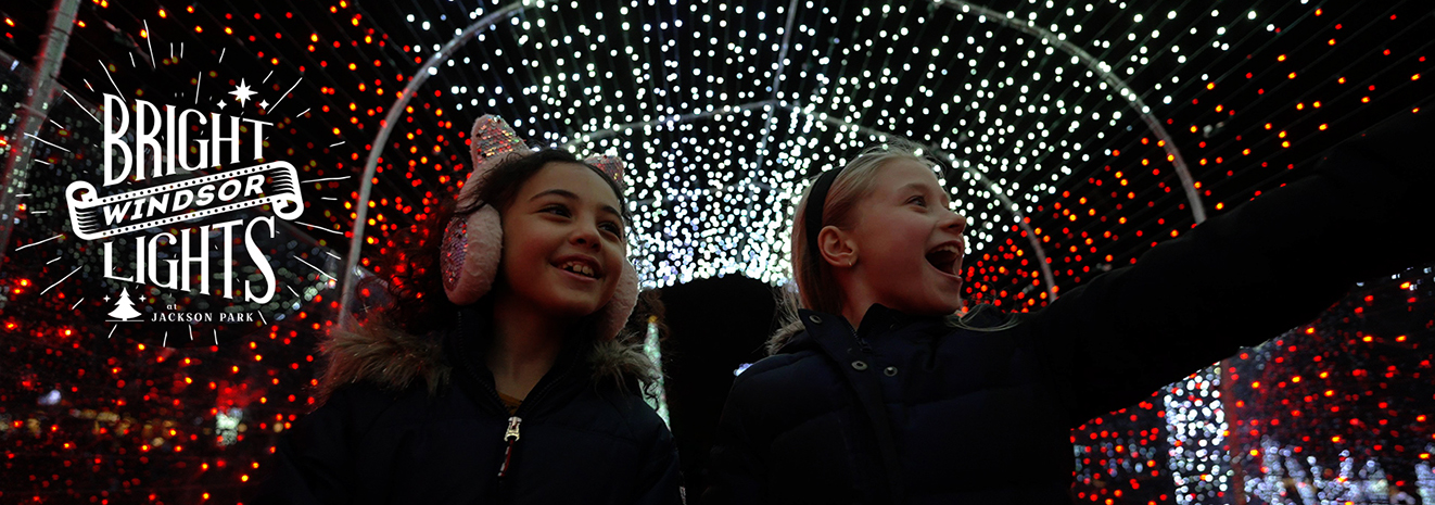 Bright Lights Windsor Logo for Bright Lights Windsor at Jackson Park and two smiling young girls in a light tunnel, one with sparkly cat earmuffs, one pointing at the lights in awe