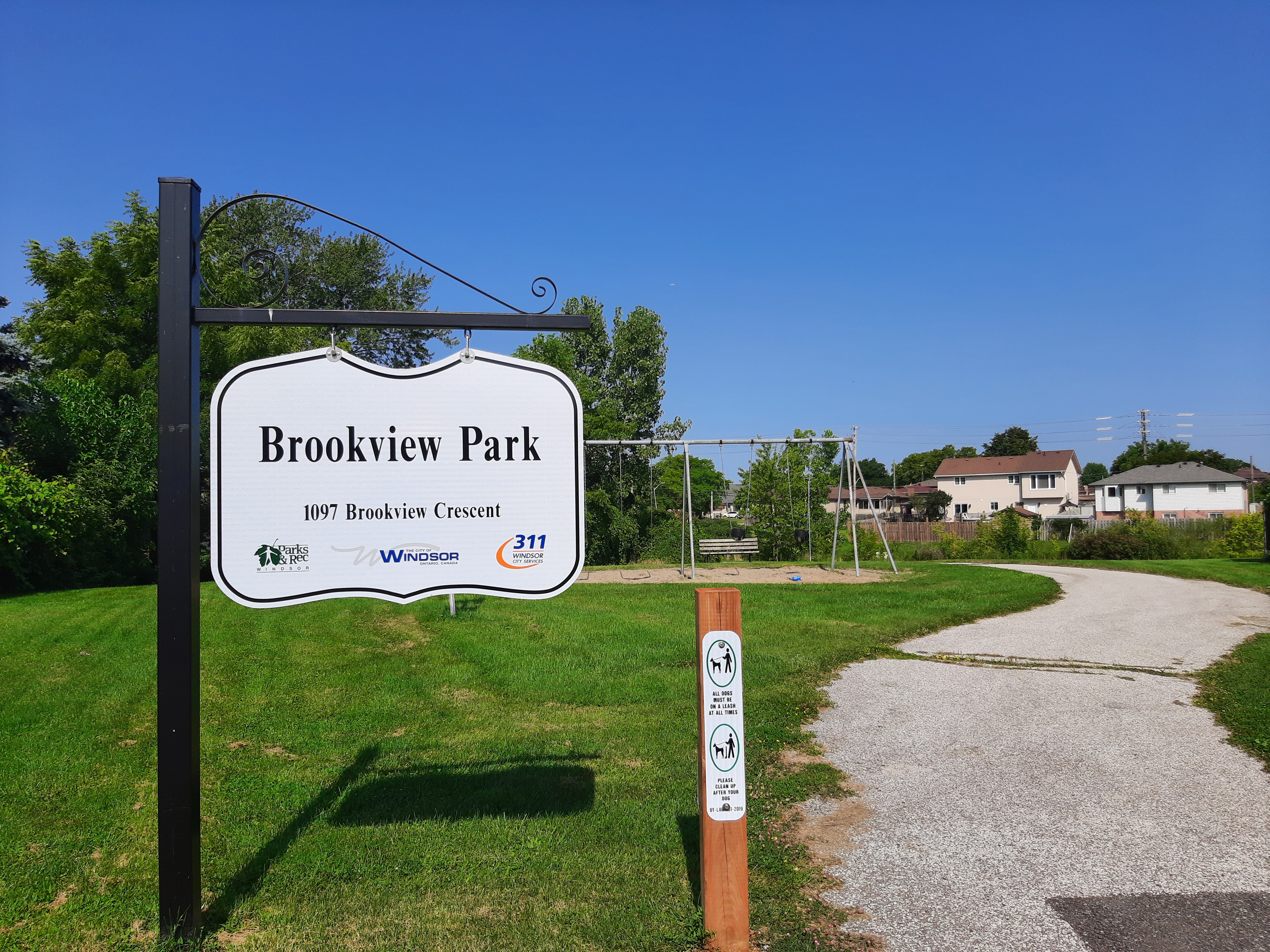 Sign for Brookview Park with swings and paved trail in background