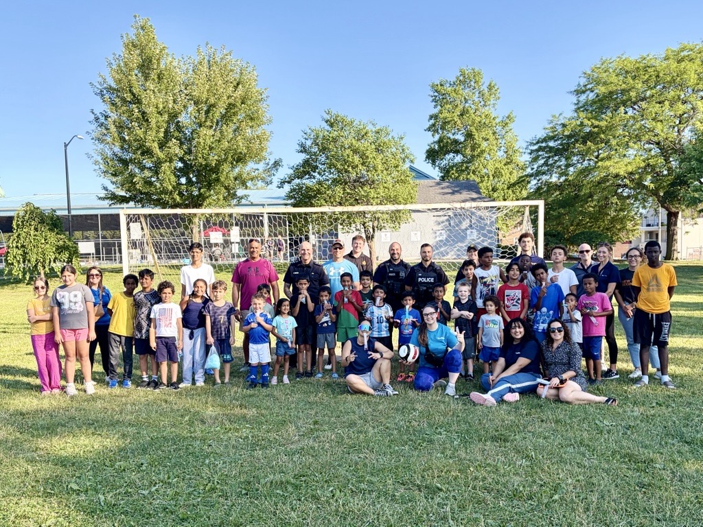 A group of youth and police officers in front of a soccer net in a park at the event Cops and Cleats